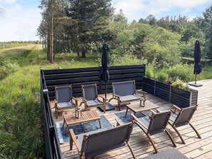 A wooden deck with a built-in seating area, including chairs and a table, surrounded by greenery and trees. - 7 Person Holiday Home in Albaek (Aalbaek)