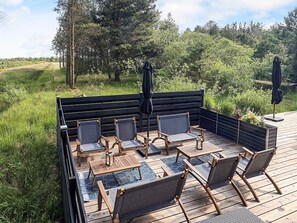 An outdoor deck with a built-in seating area, including chairs and a table, surrounded by greenery and trees. - 7 Person Holiday Home in Albaek (Aalbaek)