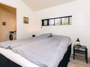 A bedroom with a large bed, a washing machine, a small table with a lamp, and a window with blinds. - 7 Person Holiday Home in Albaek (Aalbaek)