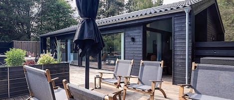 A wooden deck with outdoor furniture, a covered seating area, and a building with large windows.