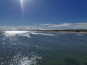 A beach with clear water reflecting sunlight, a distant shoreline, and a partly cloudy sky. - 7 Person Holiday Home in Albaek (Aalbaek)