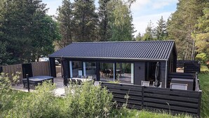 Un espace extérieur moderne, aménagé en patio, avec un coin salon abrité, un barbecue et une terrasse en bois.