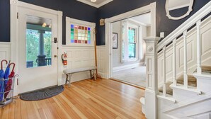 A hallway with wooden flooring, a bench, a door with a stained glass window, and a staircase with white railings. - The Avenue! Historic Mansion in DT Manitou Springs (Manitou Springs)