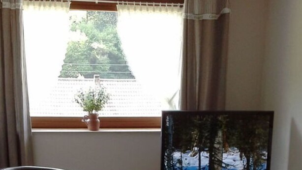 A living room with a flat-screen TV on a wooden stand, a leather chair, and a window with a view of trees and a building. - Ground Floor Palatine (Rumbach)