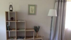 A room with a wooden bookshelf, a framed botanical illustration, a floor lamp, and a window with curtains. - Ground Floor Palatine (Rumbach)