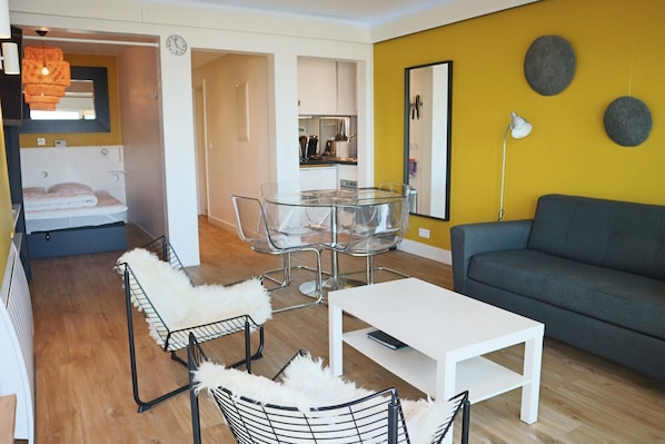 Una sala de estar moderna con una mesa de comedor de vidrio, una mesa de centro blanca y un sofá gris.