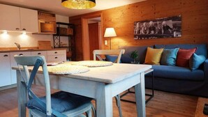 Ein gemütliches Wohnzimmer mit einer Holzvertäfelung, einem blauen Sofa und einem Esstisch mit Stühlen.