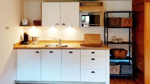 Eine kompakte Küche mit weißen Schränken, einer Holz Arbeitsplatte, einer eingebauten Mikrowelle und einem Regal mit Körben.