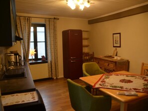 Une cuisine chaleureuse avec une table en bois, une chaise verte, un réfrigérateur rouge et une fenêtre avec des rideaux.