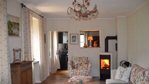 Un salon avec une cheminée, un fauteuil à motifs floraux, un canapé et un meuble en bois.