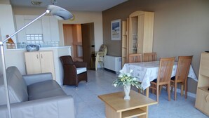 A living room with a sofa, a dining table with chairs, a wooden cabinet, and a lamp. - Studio in Nieuwpoort With Stunning Sea View (Nieuwpoort)