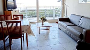 A modern living room with a sofa, dining table, chairs, a TV, and a balcony with a railing. - Studio in Nieuwpoort With Stunning Sea View (Nieuwpoort)