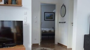 A living room with a TV, a red chair, a wooden table, and a small table with a plate and a glass. - Holiday Apartment Windrose (Boergerende-Rethwisch)