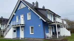 A two-story house with a blue exterior, white trim, and a balcony on the second floor. - Holiday Apartment Windrose (Boergerende-Rethwisch)
