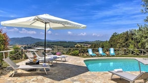 A poolside area with lounge chairs, a white umbrella, and a view of the countryside. - Villa Morotti Comfortable Holiday Residence (Montone)