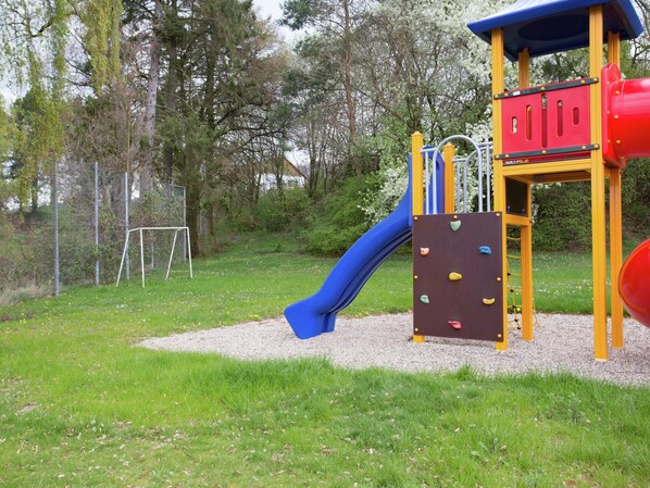 Une aire de jeux avec un toboggan, un mur d’escalade et une structure de jeu rouge et jaune.