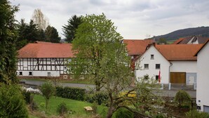 A traditional half-timbered house with a red-tiled roof, surrounded by lush greenery and a small pond.