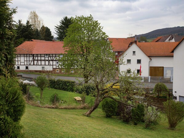 Une maison traditionnelle à colombages, surmontée d’un toit de tuiles rouges, entourée d’une végétation luxuriante et d’un petit étang.