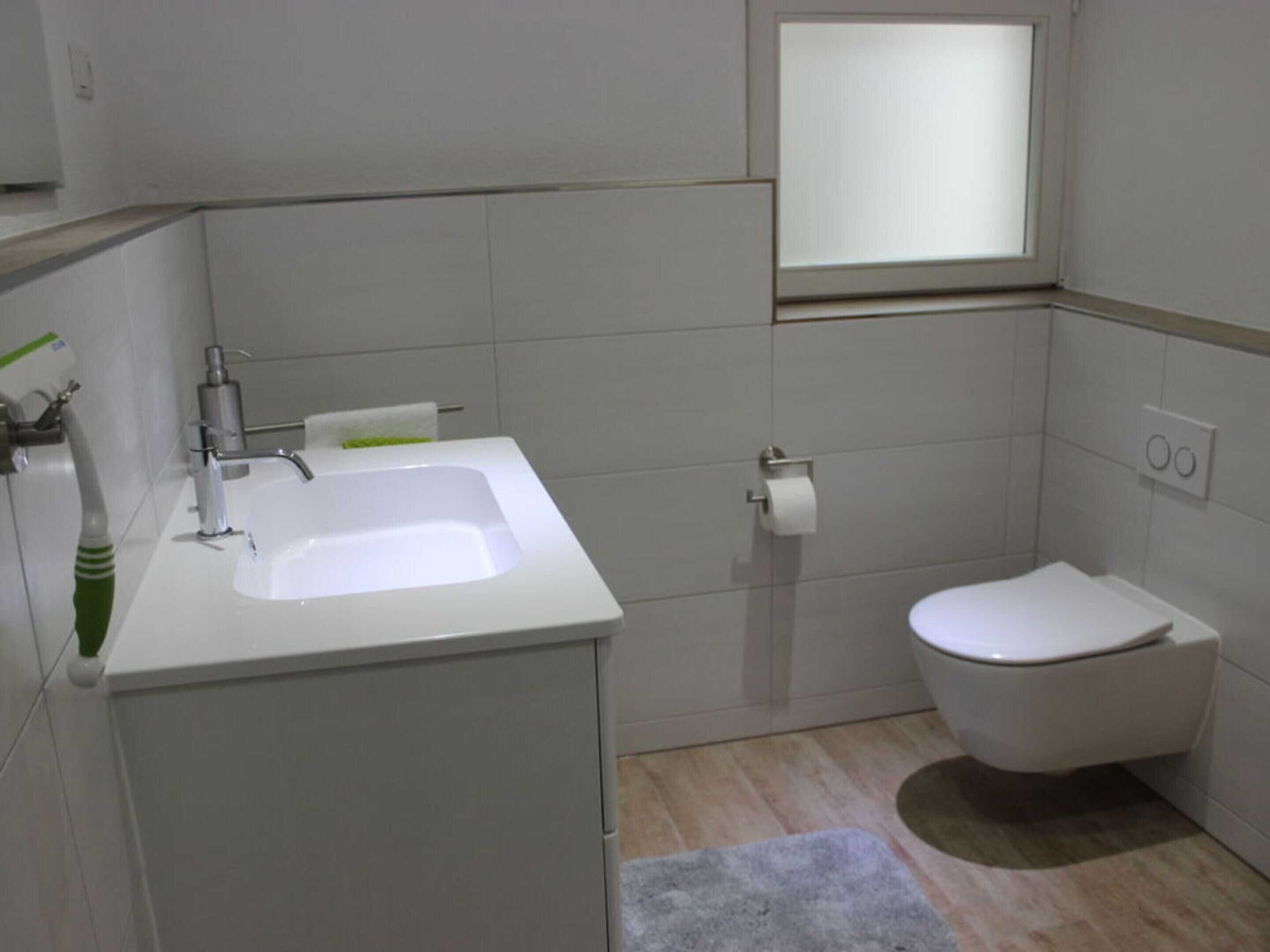A modern bathroom with a white sink, toilet, and a small window.