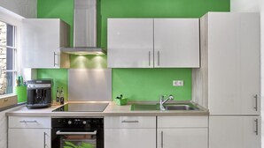 A modern kitchen with white cabinets, a stainless steel range hood, a built-in oven, a coffee maker, and a green backsplash. - In the Rhein-mosel Holiday Home (Brodenbach)