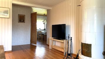 A living room with a wooden floor, a television on a stand, a fireplace, and a dining area in the background.