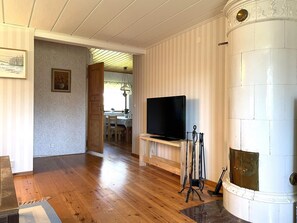 A living room with a wooden floor, a television on a stand, a fireplace, and a dining area in the background. - 5 Person Holiday Home in Ulrika (Ulrika)