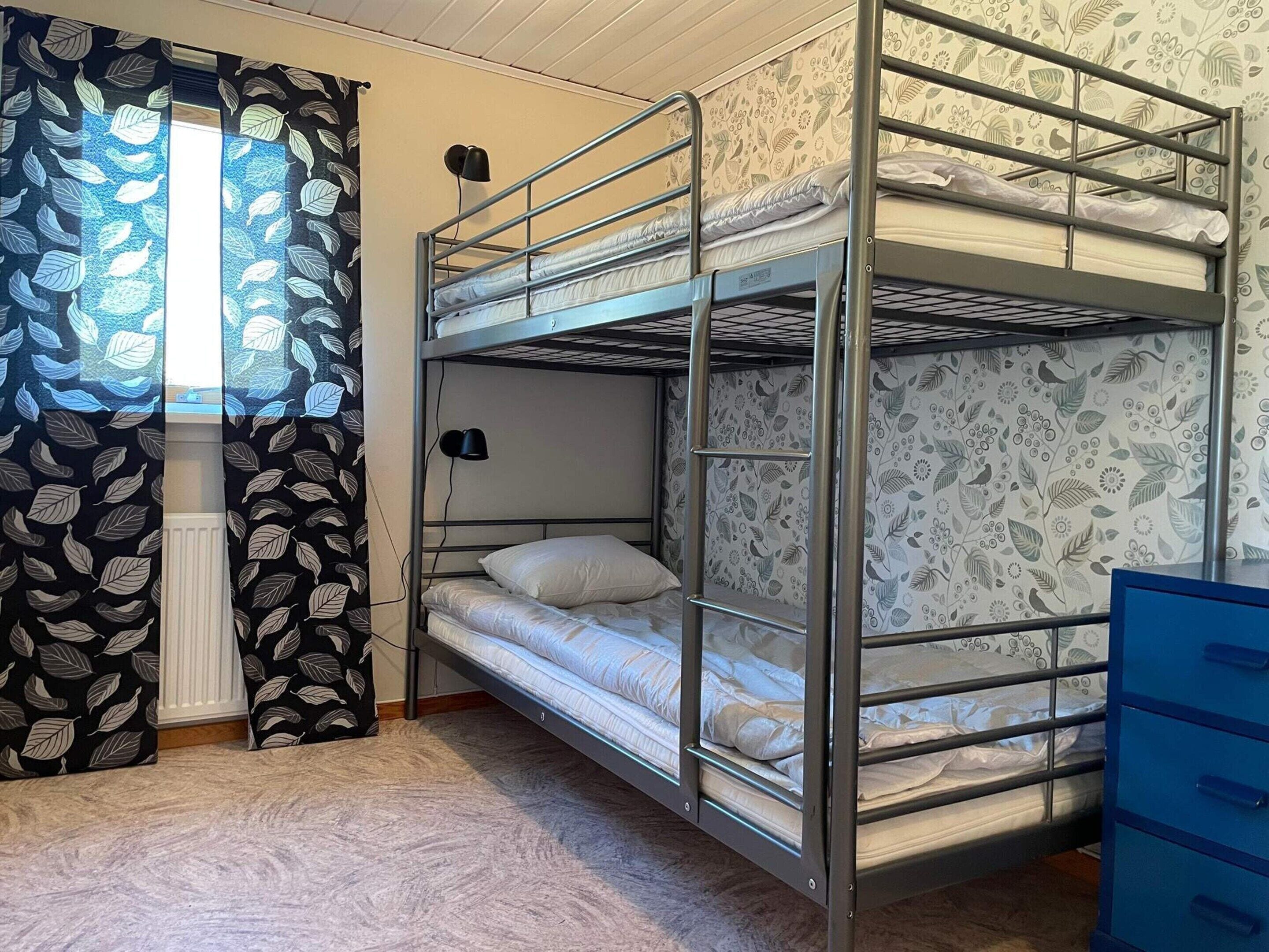 A bunk bed room with a patterned curtain, a radiator, and a blue dresser.