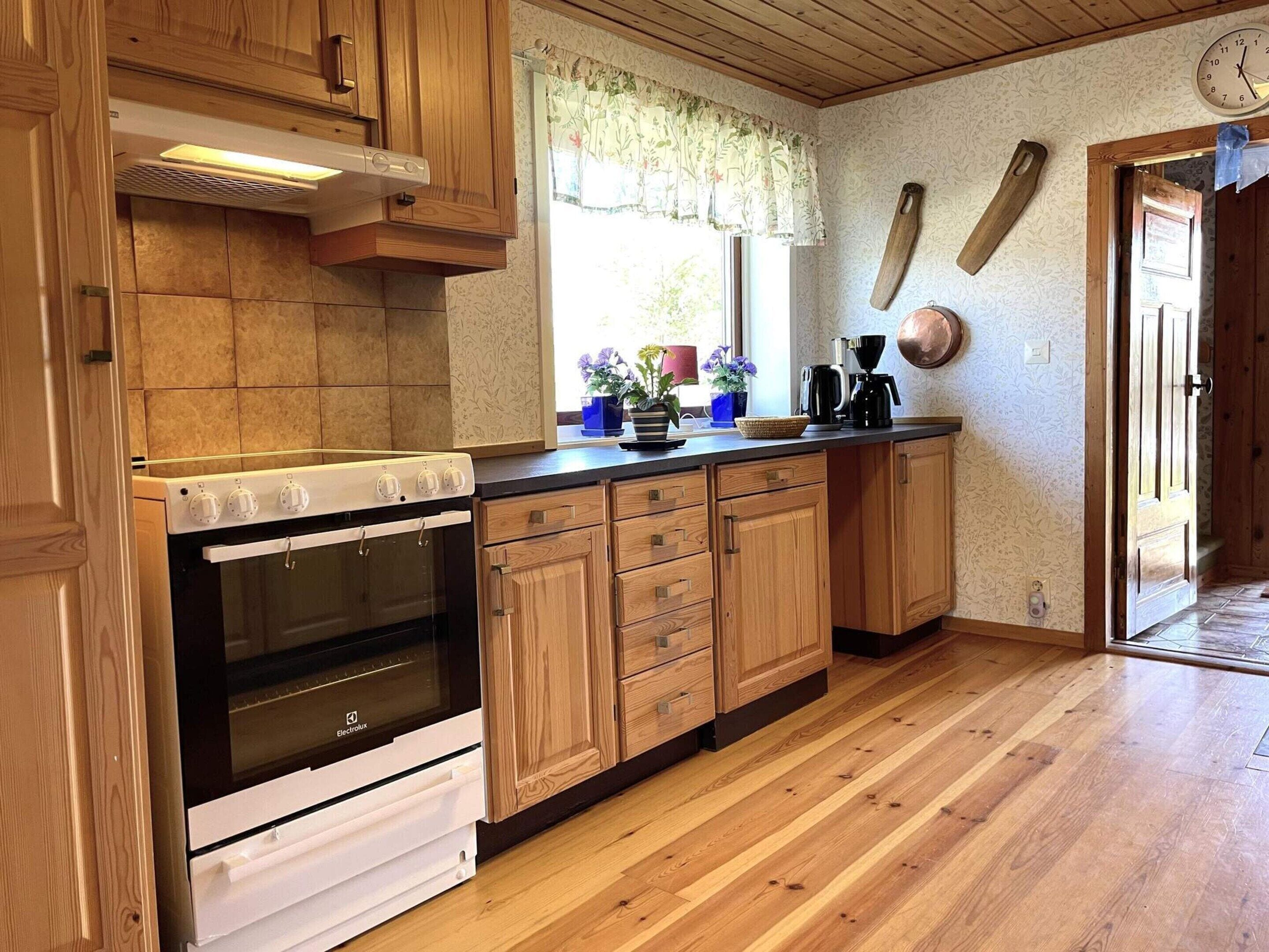 A kitchen with wooden cabinets, a white stove, and a window with floral curtains.
