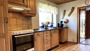 A kitchen with wooden cabinets, a white stove, and a window with floral curtains. - 5 Person Holiday Home in Ulrika (Ulrika)