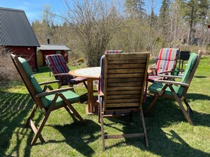 A wooden table with four chairs, each with a green cushion, in a grassy outdoor area with a red building in the background. - 5 Person Holiday Home in Ulrika-by Traum (Ulrika)