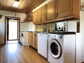 A kitchen with wooden cabinets, a washing machine, a microwave, and a sink. - 5 Person Holiday Home in Ulrika (Ulrika)