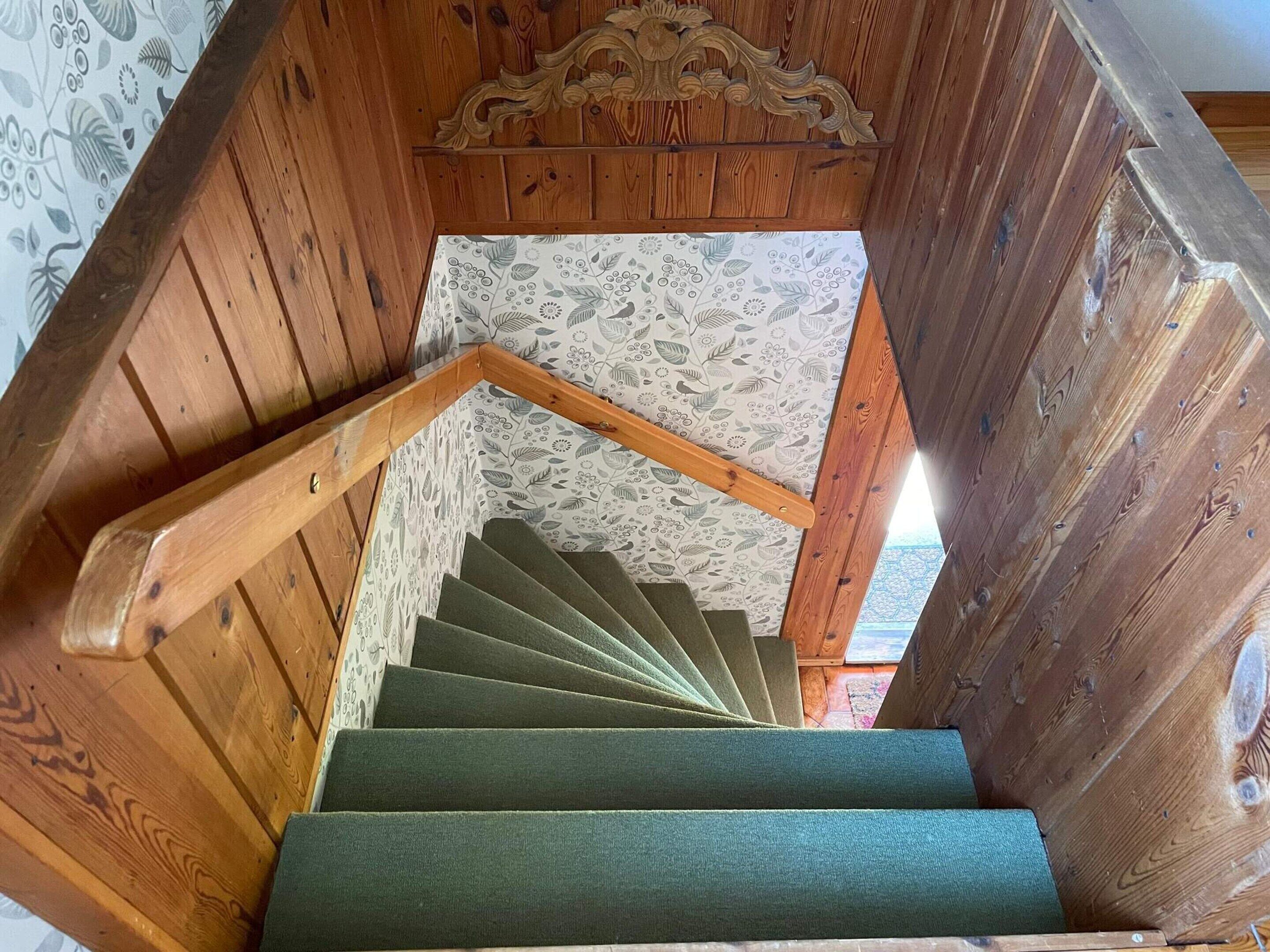 A wooden staircase with a green carpeted handrail and a floral-patterned wall.