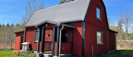 Una casa de madera roja con techo gris, chimenea y porche.