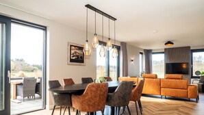 Un comedor moderno con suelo de parqué de madera, una mesa de madera oscura y sillas de cuero marrón. Se aprecia un amplio ventanal con vistas al exterior.