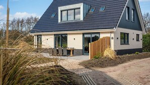 Una casa moderna con techo inclinado, ventanas amplias y un patio con mobiliario exterior.