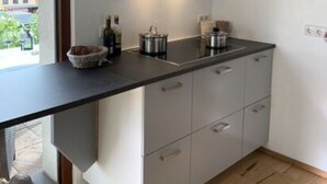 A modern kitchen with a black range hood, a countertop with a kettle, and a window overlooking a garden. - Holiday Apartment by the Pond (Kamp-Bornhofen)
