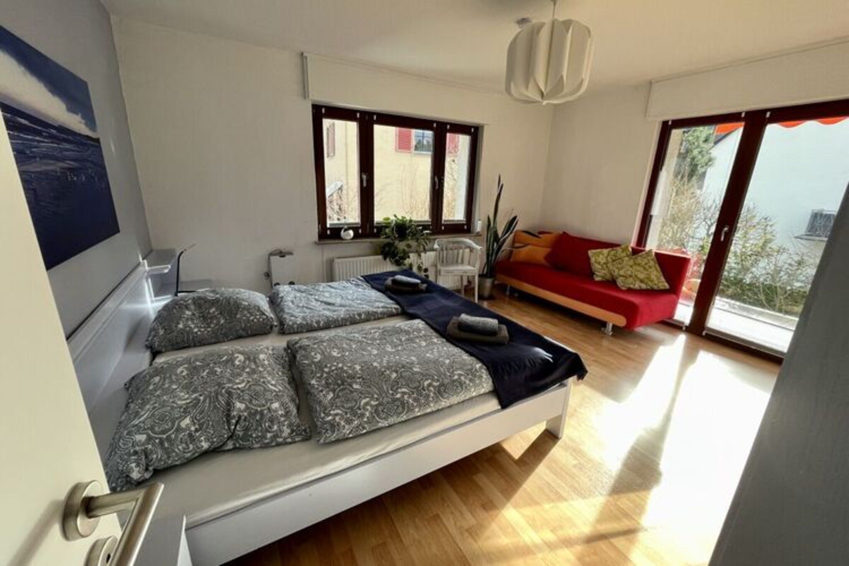 A modern bedroom with a bed, a red sofa, and a large window.
