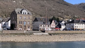 A riverside town with traditional buildings, a sign reading "KAMP-BORNHOFEN," and a hilly backdrop. - Holiday Apartment by the Pond (Kamp-Bornhofen)