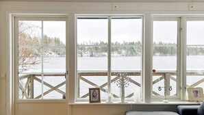 A room with a large window overlooking a body of water, a wooden floor, and a grey sofa. - 4 Star Holiday Home in Stensjon (Stensjon)