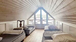 A loft bedroom with a sloped ceiling, wooden beams, and a large skylight. There are two beds with mattresses and pillows. - 4 Star Holiday Home in Stensjon (Stensjon)