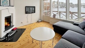 A living room with a fireplace, a flat-screen TV, a round table, and a sofa. - 4 Star Holiday Home in Stensjon (Stensjon)