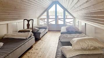 A loft bedroom with a sloped ceiling, wooden beams, and a large skylight. There are two beds and a bench.