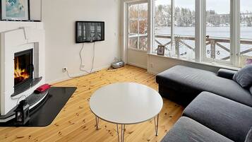 A living room with a fireplace, a television, a sofa, and a view of a snowy landscape through large windows.
