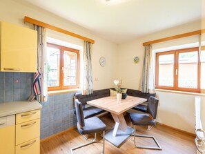 A compact kitchen with a dining area, featuring a wooden table, two chairs, a small potted plant, and a clock on the wall. - Apartment in Piesendorf Near Ski Slopes (Piesendorf)