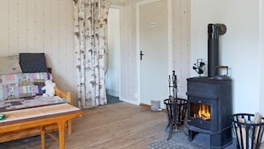 Et hyggeligt værelse med trægulv, en seng med et quiltet dynebetræk, en pejs og gardiner med et naturmotiv.