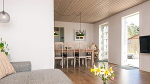 A modern living room with a grey sofa, a round wooden coffee table with a vase of flowers, and a dining area with wooden chairs and a green pendant light. - 8 Person Holiday Home in Bjert (Bjert)