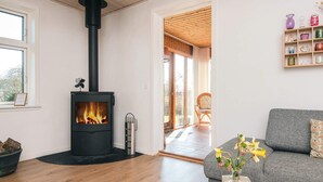 A living room with a wood-burning stove, a grey sofa, a wooden coffee table, and a vase with flowers. - 8 Person Holiday Home in Bjert (Bjert)