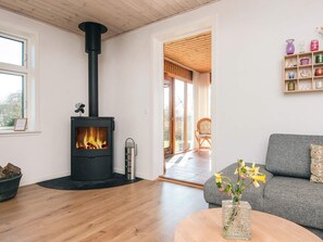 Ein Wohnzimmer mit Kaminofen, grauem Sofa, Holztisch und Blumenvase.