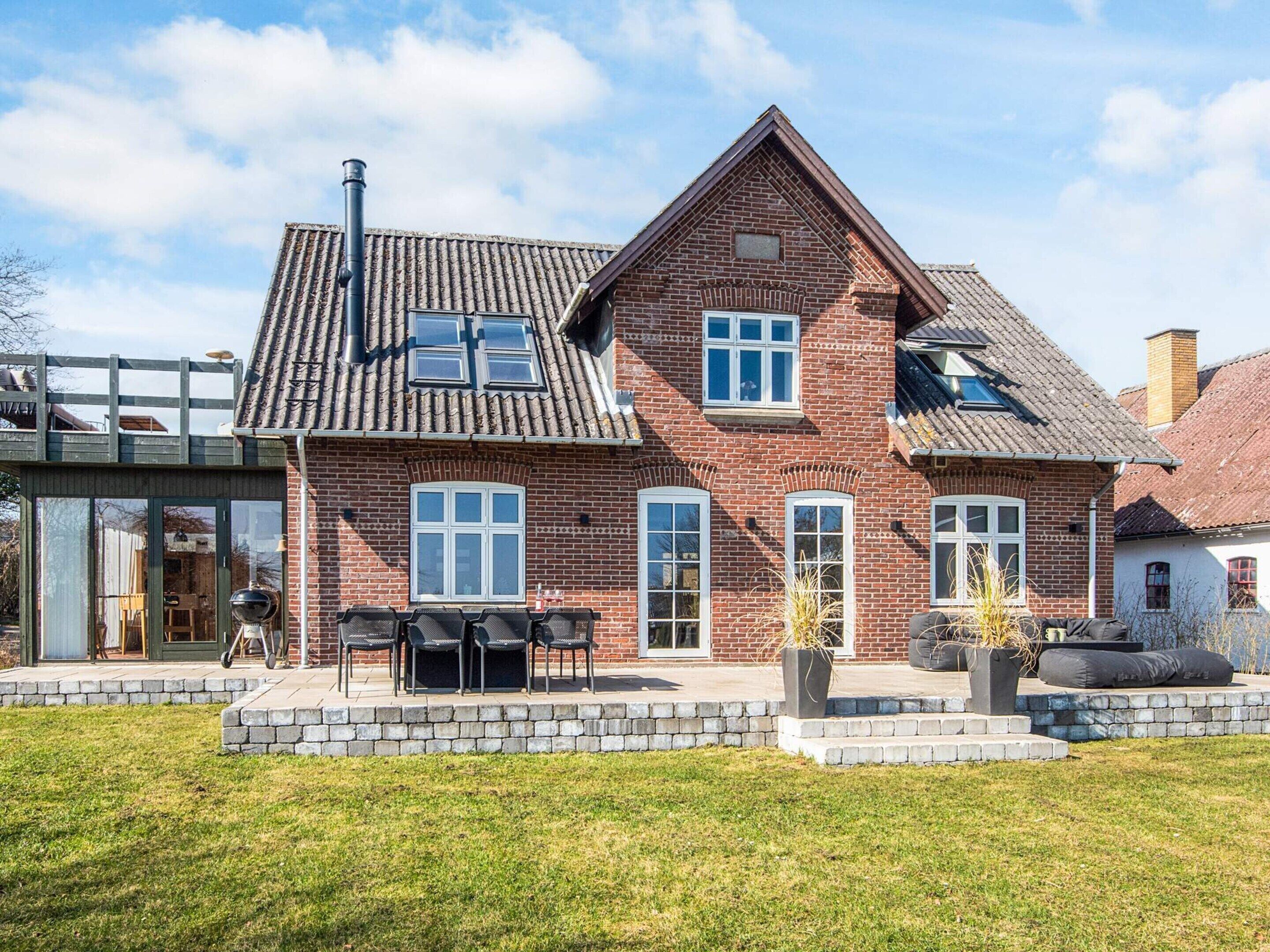 Une maison à deux étages, construite en briques, avec un toit en tuiles, un balcon et un patio aménagé avec du mobilier d’extérieur.
