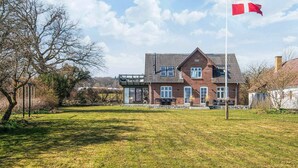 A large brick house with a sloped roof, a flagpole with a flag, and a grassy yard. - 8 Person Holiday Home in Bjert (Bjert)